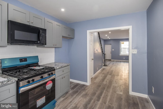 kitchen featuring stainless steel gas stove, gray cabinetry, backsplash, light stone counters, and dark hardwood / wood-style flooring