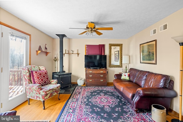 living room featuring a wood stove, a textured ceiling, wood-type flooring, and ceiling fan