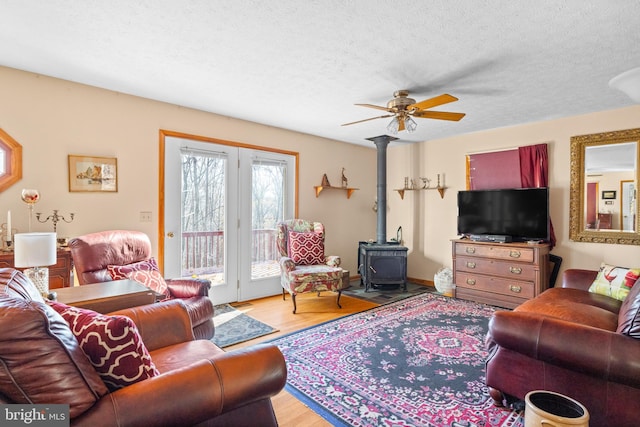 living room featuring light wood-type flooring, a wood stove, ceiling fan, and a textured ceiling