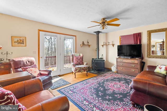 living room featuring light wood-type flooring, ceiling fan, a textured ceiling, and a wood stove