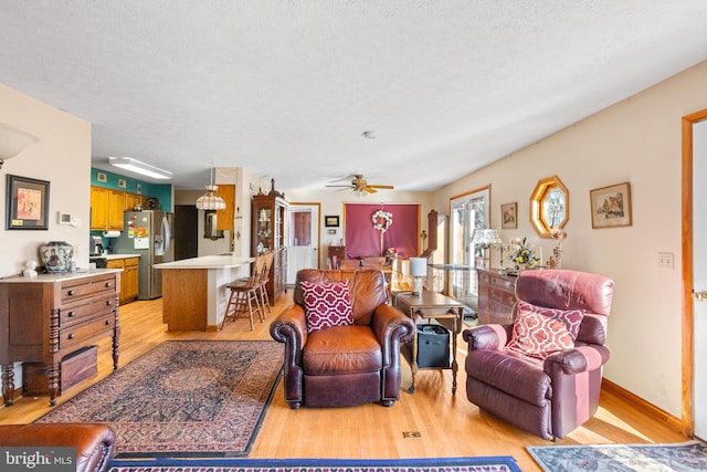 living room with light hardwood / wood-style floors, ceiling fan, and a textured ceiling