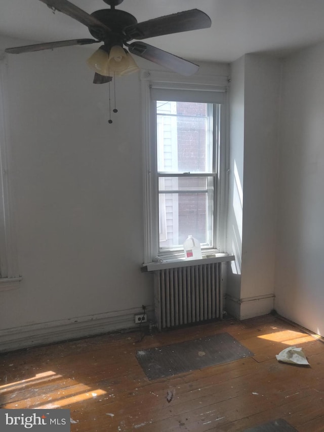 empty room featuring ceiling fan, wood-type flooring, and radiator heating unit