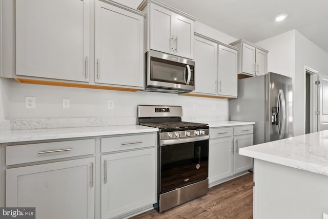 kitchen featuring dark wood-type flooring, stainless steel appliances, light stone countertops, and gray cabinetry