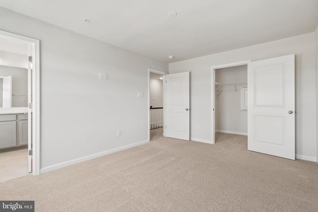 unfurnished bedroom featuring a spacious closet, connected bathroom, light colored carpet, and a closet