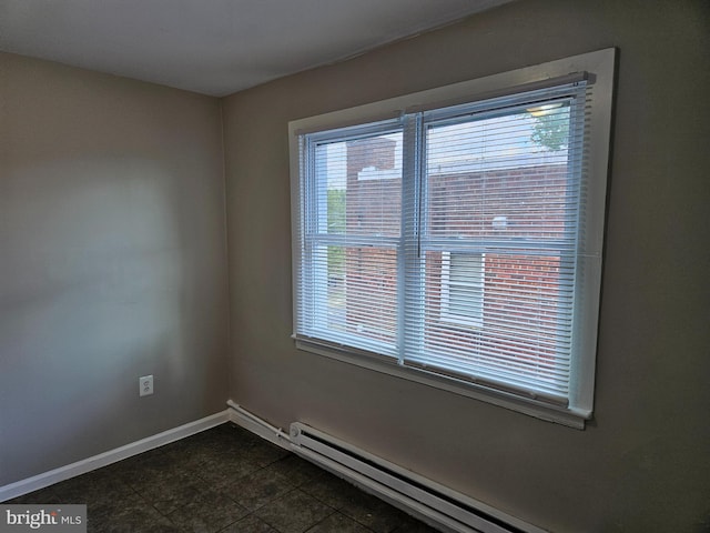 empty room featuring dark tile patterned flooring, a wealth of natural light, and baseboard heating