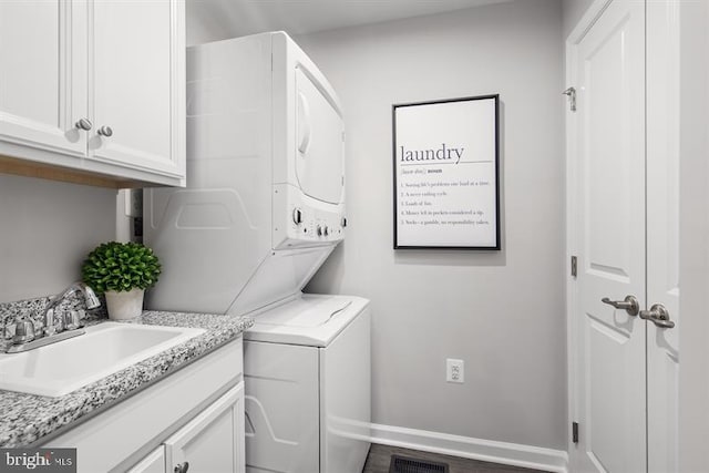 washroom featuring sink, stacked washer and clothes dryer, wood-type flooring, and cabinets