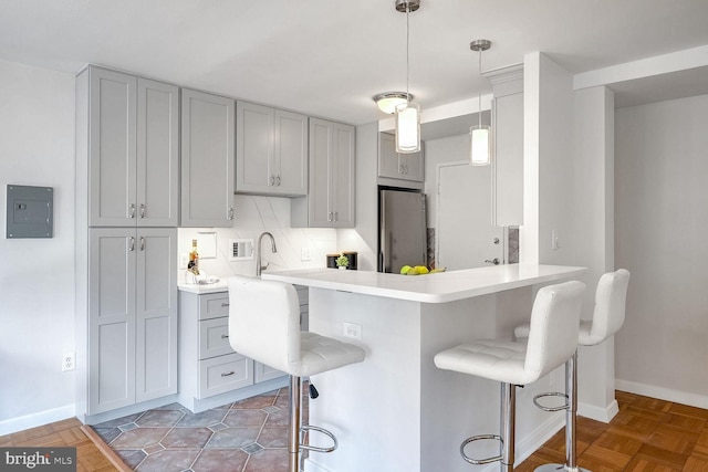 kitchen with kitchen peninsula, a kitchen bar, stainless steel refrigerator, pendant lighting, and gray cabinets