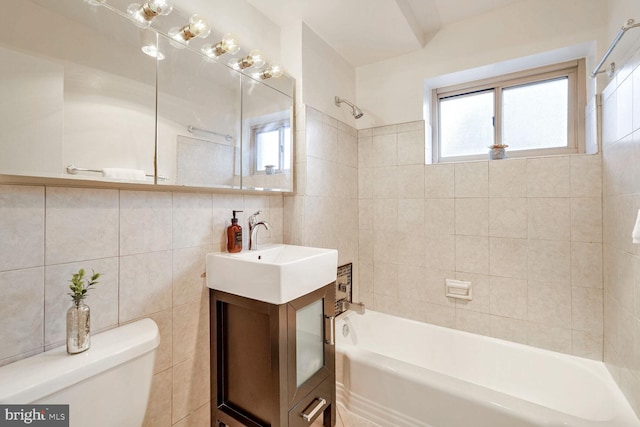 full bathroom featuring toilet, tiled shower / bath combo, vanity, and tile walls