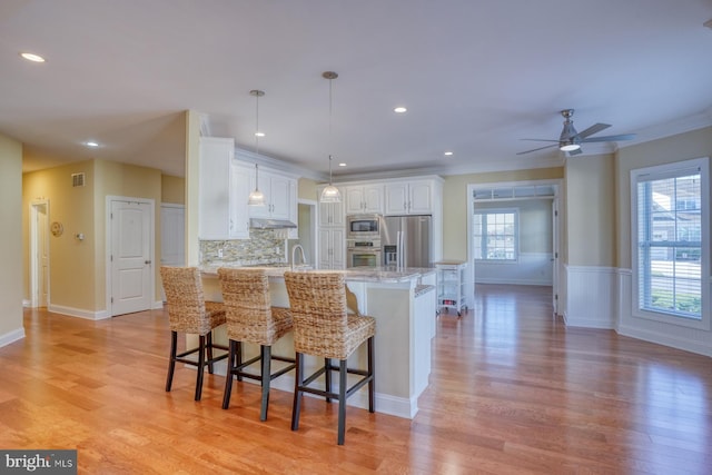 kitchen featuring appliances with stainless steel finishes, white cabinetry, light stone countertops, light hardwood / wood-style floors, and decorative light fixtures