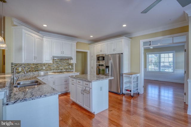 kitchen with appliances with stainless steel finishes, sink, light wood-type flooring, a kitchen island, and hanging light fixtures