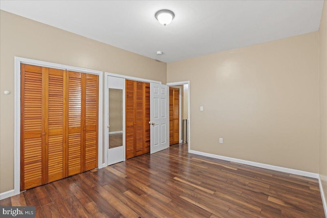 unfurnished bedroom with multiple closets and dark wood-type flooring