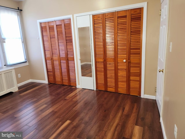 unfurnished bedroom featuring multiple windows, dark hardwood / wood-style flooring, and two closets