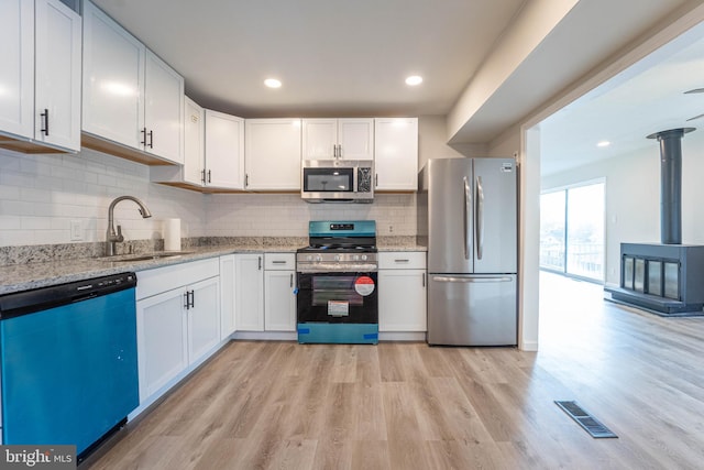 kitchen with light stone countertops, sink, stainless steel appliances, white cabinets, and light hardwood / wood-style flooring