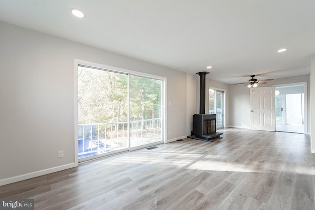 unfurnished living room featuring a wood stove, light wood-type flooring, and ceiling fan