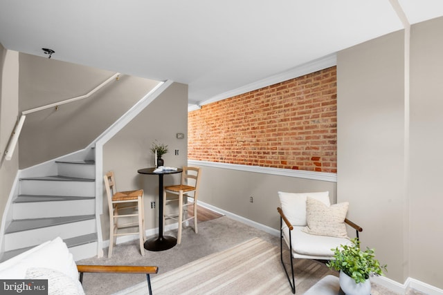 living area featuring brick wall, crown molding, and carpet floors