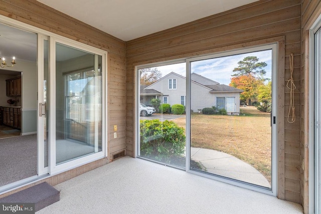 doorway with a healthy amount of sunlight, wooden walls, and carpet