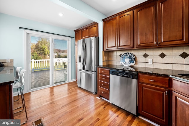 kitchen with appliances with stainless steel finishes, tasteful backsplash, dark stone countertops, beam ceiling, and light wood-type flooring