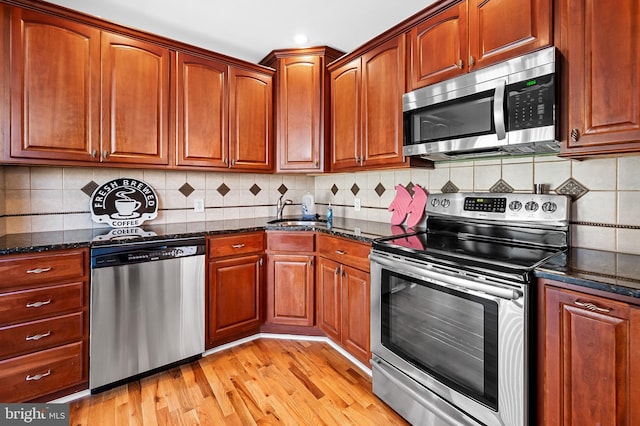 kitchen featuring appliances with stainless steel finishes, light hardwood / wood-style floors, tasteful backsplash, and dark stone countertops