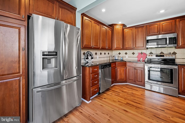 kitchen featuring stainless steel appliances, light wood-type flooring, sink, decorative backsplash, and dark stone countertops