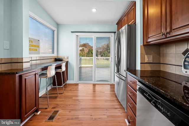 kitchen featuring backsplash, dark stone countertops, light wood-type flooring, and appliances with stainless steel finishes