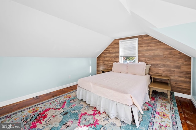 bedroom with dark hardwood / wood-style floors, wooden walls, and lofted ceiling