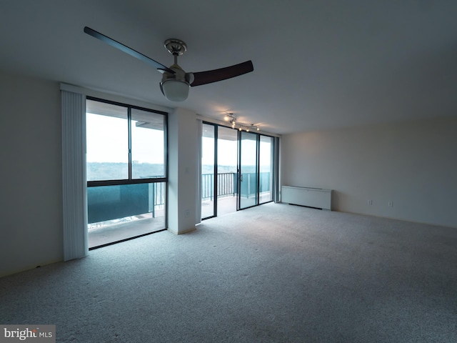 empty room featuring ceiling fan, radiator heating unit, floor to ceiling windows, a water view, and light colored carpet