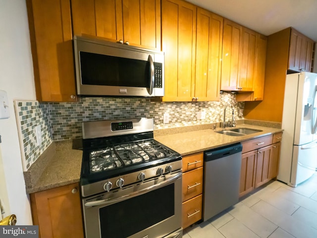 kitchen with tasteful backsplash, light stone countertops, appliances with stainless steel finishes, and sink