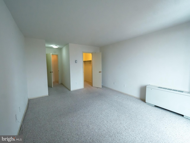 unfurnished bedroom with a walk in closet, radiator heating unit, light colored carpet, and a closet