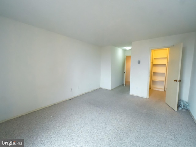 unfurnished bedroom featuring a spacious closet, light carpet, and a closet