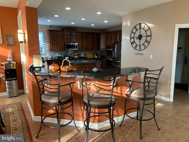 kitchen featuring a kitchen bar, kitchen peninsula, backsplash, and black refrigerator with ice dispenser