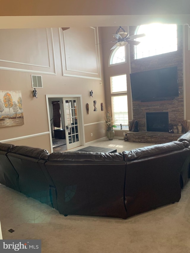 living room with a stone fireplace, ceiling fan, and carpet