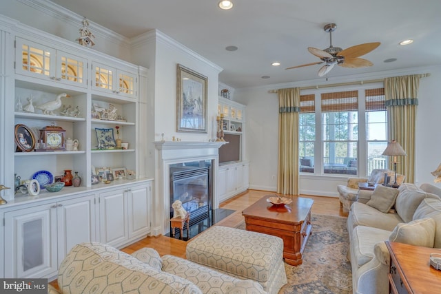 living room with crown molding, recessed lighting, light wood-style flooring, a fireplace with flush hearth, and a ceiling fan