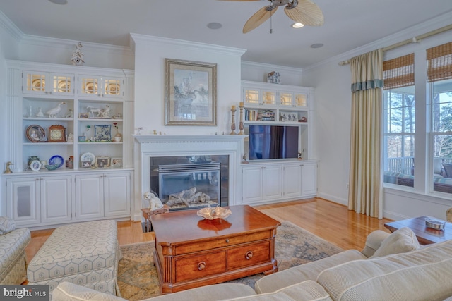 living room with light wood-style floors, a glass covered fireplace, and crown molding