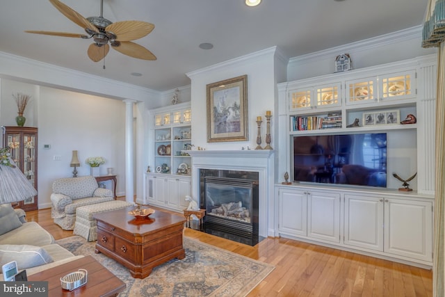 living room with built in shelves, light wood finished floors, ornamental molding, a fireplace with flush hearth, and a ceiling fan