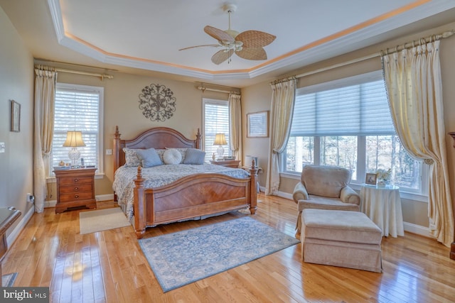 bedroom featuring ornamental molding, a tray ceiling, baseboards, and light wood finished floors