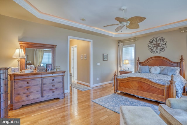 bedroom with light wood-type flooring, a tray ceiling, crown molding, and baseboards