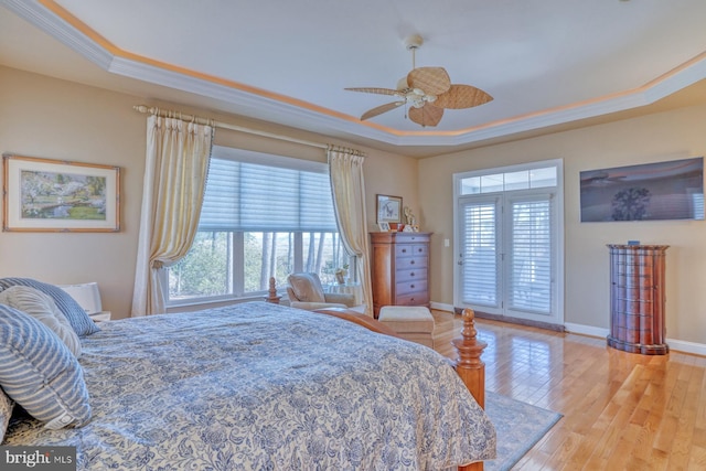 bedroom featuring light wood-style flooring, multiple windows, a tray ceiling, and ornamental molding