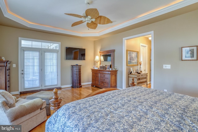 bedroom with ornamental molding, a tray ceiling, baseboards, and wood finished floors