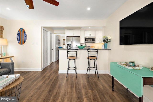 kitchen with a kitchen bar, stainless steel appliances, dark wood-type flooring, white cabinets, and kitchen peninsula