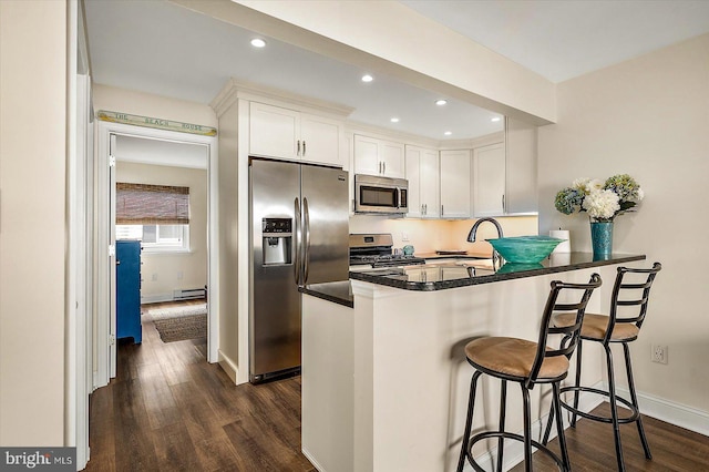 kitchen featuring dark hardwood / wood-style flooring, kitchen peninsula, a breakfast bar, white cabinetry, and appliances with stainless steel finishes