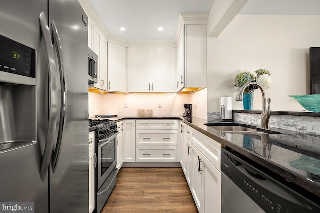 kitchen featuring dark wood-type flooring, dark stone counters, white cabinets, sink, and appliances with stainless steel finishes