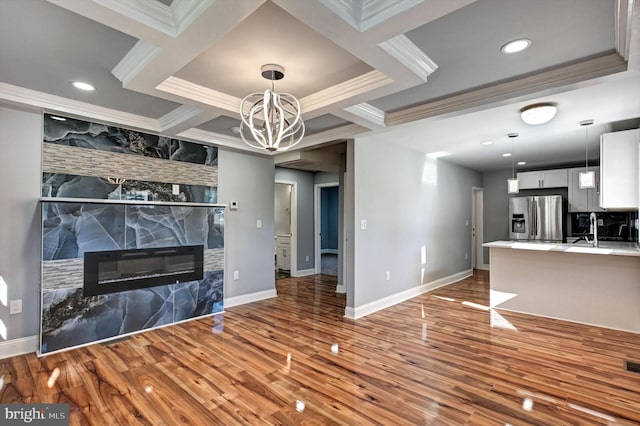 unfurnished living room with wood-type flooring, a chandelier, a stone fireplace, and ornamental molding