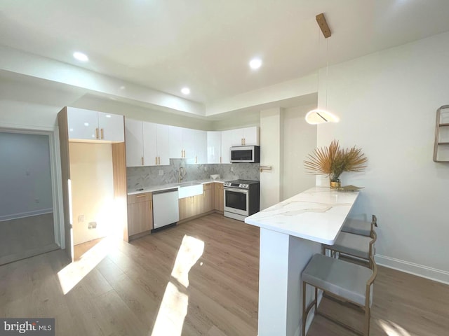 kitchen featuring kitchen peninsula, appliances with stainless steel finishes, white cabinetry, light hardwood / wood-style flooring, and pendant lighting