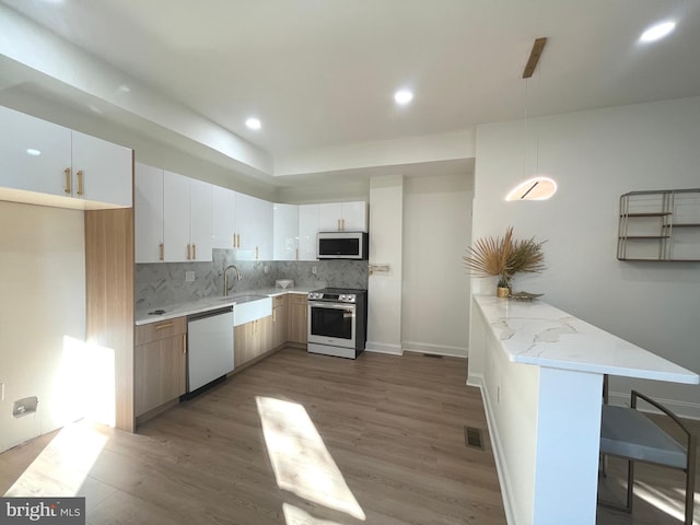 kitchen featuring appliances with stainless steel finishes, a kitchen bar, kitchen peninsula, white cabinets, and dark hardwood / wood-style floors