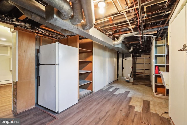 basement with baseboard heating, wood-type flooring, and white fridge