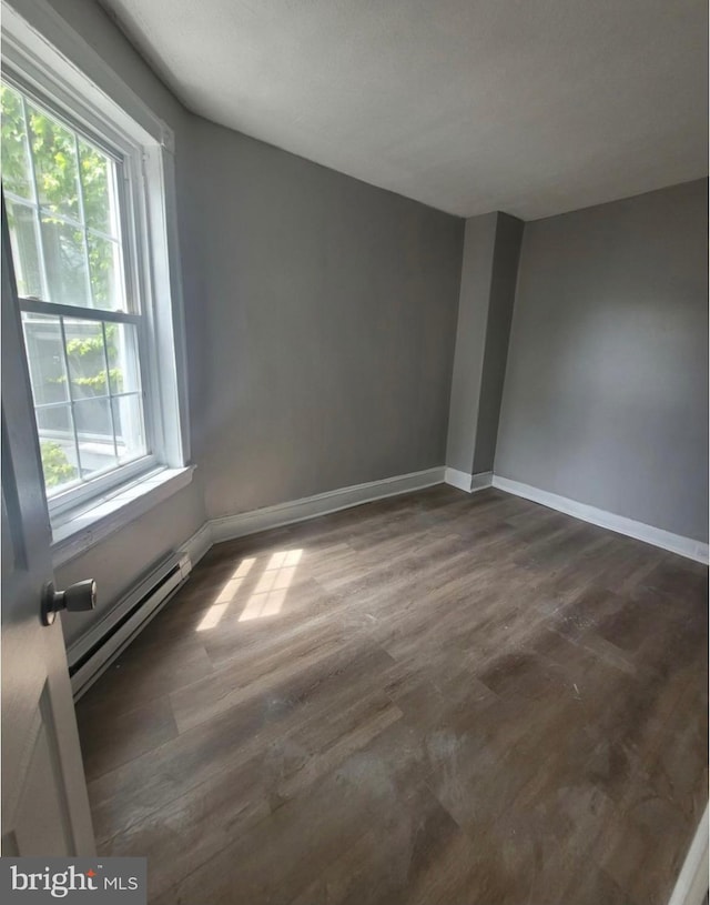 unfurnished room with a baseboard heating unit and dark hardwood / wood-style flooring