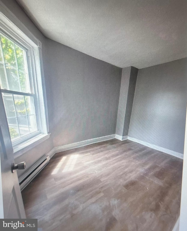 spare room featuring hardwood / wood-style flooring, baseboard heating, and a textured ceiling