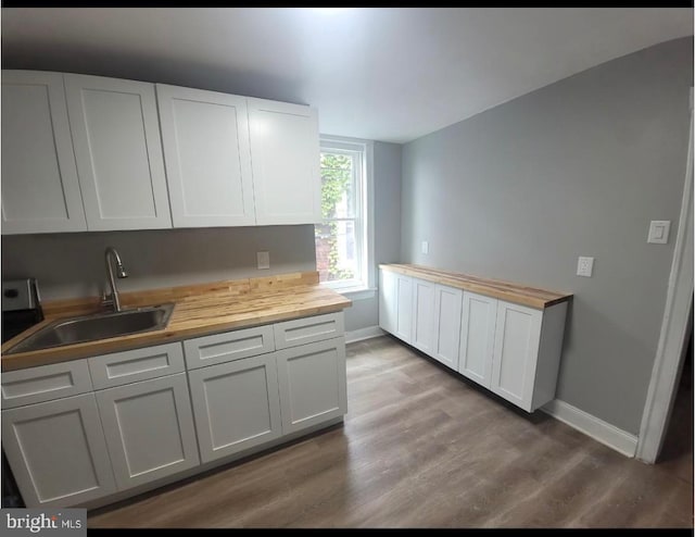 kitchen featuring butcher block counters, sink, hardwood / wood-style flooring, and white cabinets