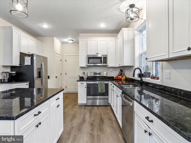 kitchen featuring white cabinets, hanging light fixtures, wood-type flooring, sink, and stainless steel appliances