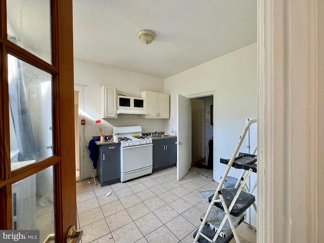 kitchen with sink, tasteful backsplash, white range with gas stovetop, cream cabinetry, and light tile patterned flooring